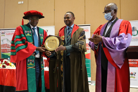 The Deputy Vice Chancellor (Academic Affairs) Dr. Umar Kakumba (2nd) hands over another  certificate in commemoration of the inaugural lecture to Edward Bbaale (L) flanked by the Chair Professorial Inaugural Committee Prof. Elly Sabiiti