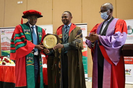The Deputy Vice Chancellor (Academic Affairs) Dr. Umar Kakumba (2nd) hands over another  certificate in commemoration of the inaugural lecture to Edward Bbaale (L) flanked by the Chair Professorial Inaugural Committee Prof. Elly Sabiiti