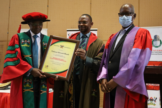 The Deputy Vice Chancellor (Academic Affairs) Dr. Umar Kakumba (2nd) hands over the a certificate in commemoration of the inaugural lecture to Edward Bbaale (L) flanked by the Chair Professorial Inaugural Committee Prof. Elly Sabiiti