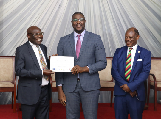 One of the graduands (c) receives the certificate from the minister(L) witness by Barnabas Nawangwe.